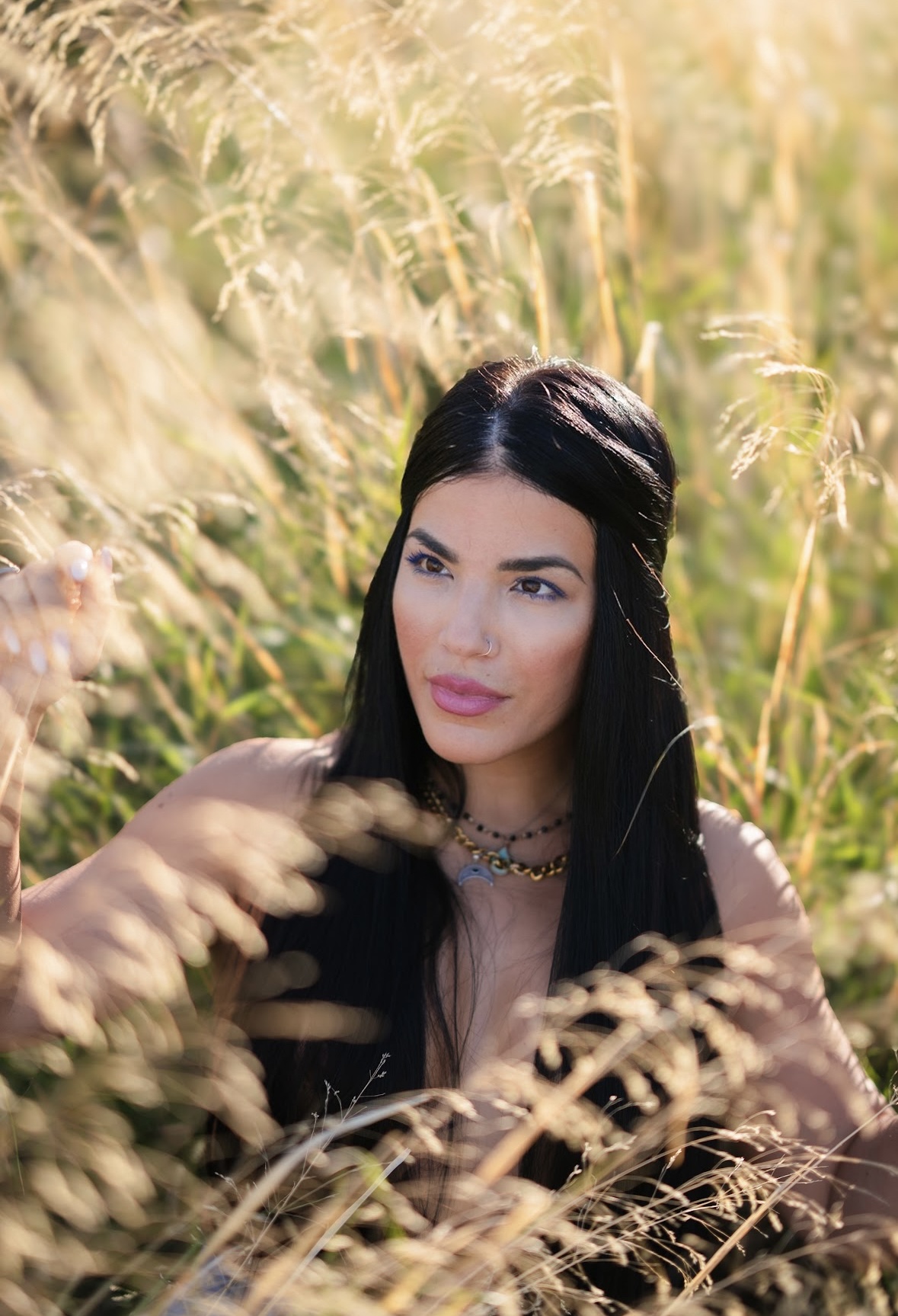 Woman with long dark hair and necklace in a field of tall golden grass.
