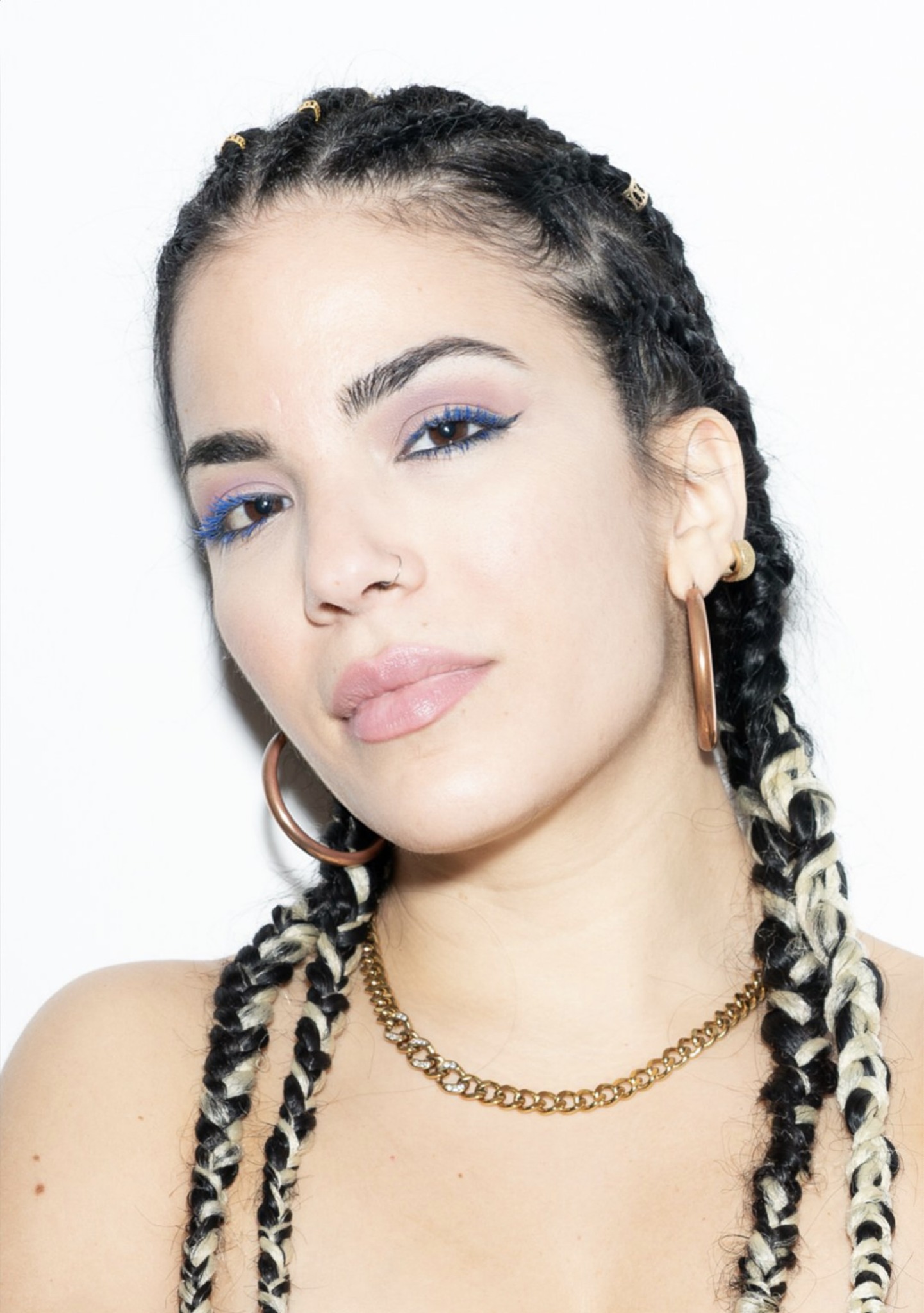 Young woman with braided hair, hoop earrings, and a gold necklace, looking confidently at the camera.