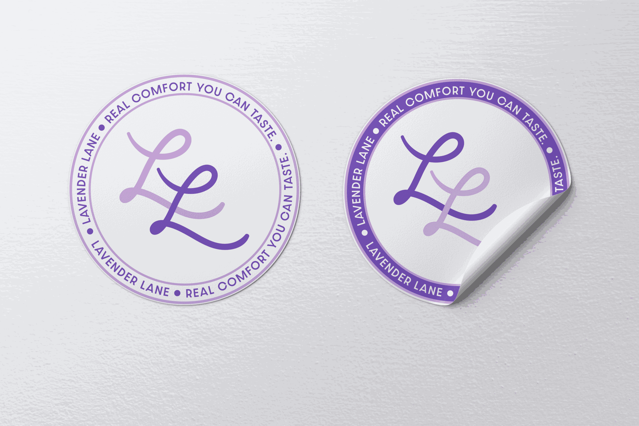 Two circular stickers with purple borders and text, one with a curled corner, on a light gray surface.