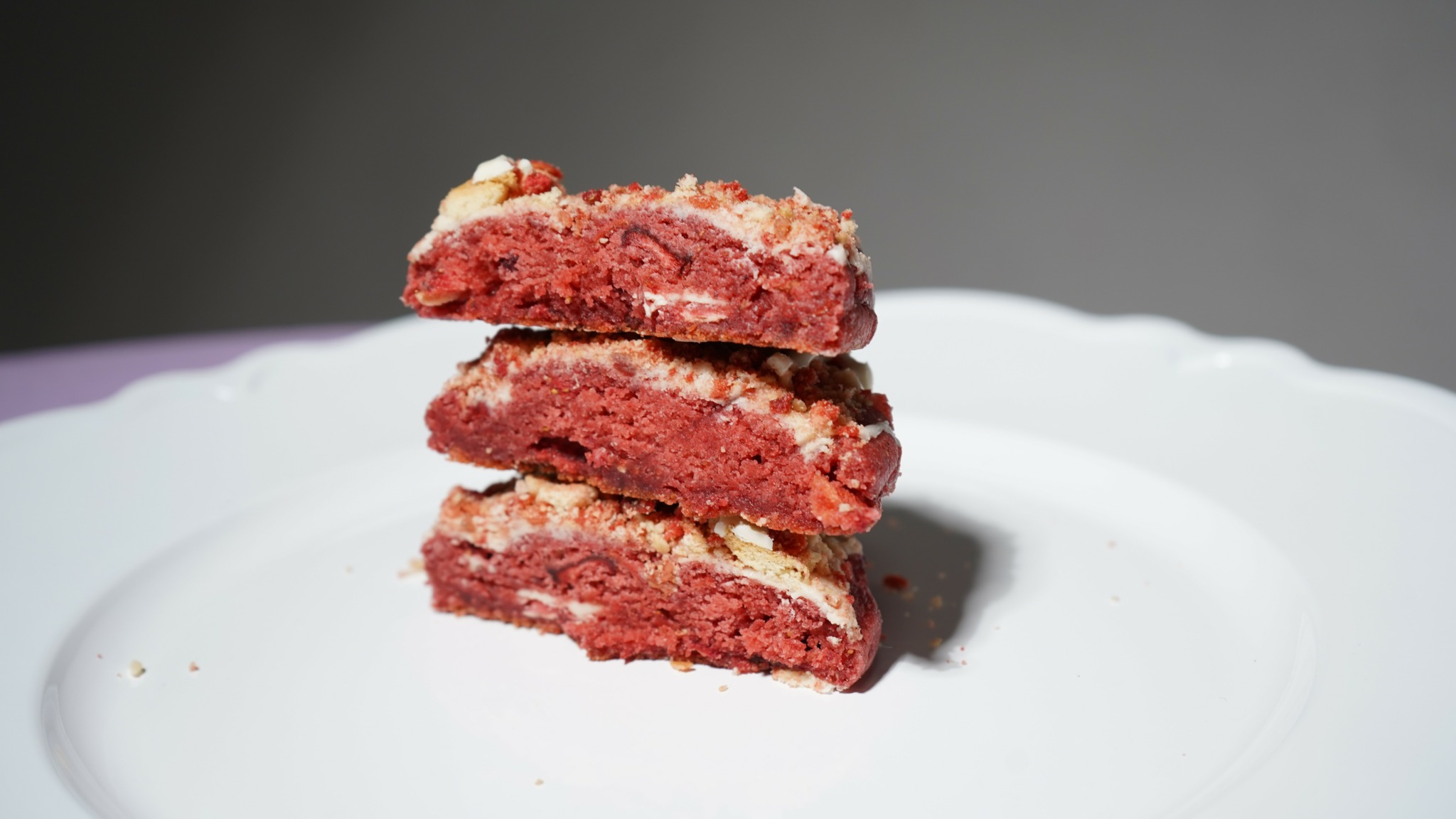 Stack of three red and beige layered bars on a white plate against a dark background.