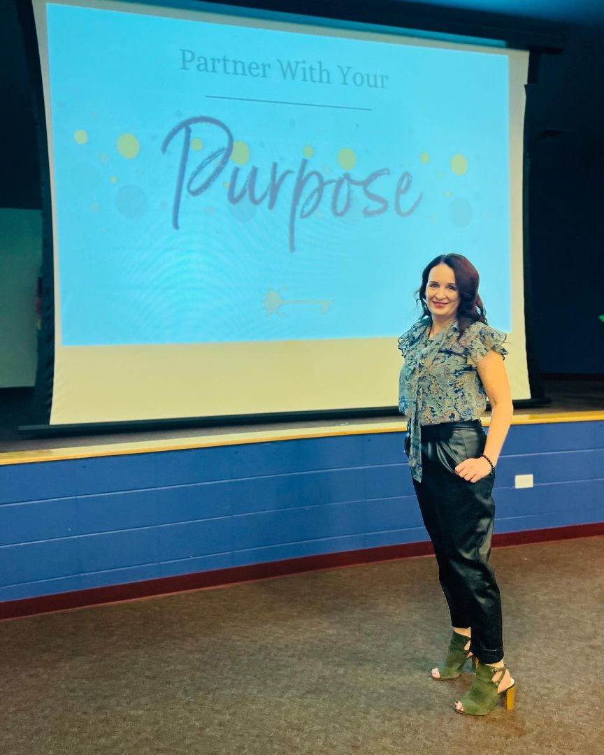 Woman standing in front of a presentation slide that reads 'Partner With Your Purpose'.