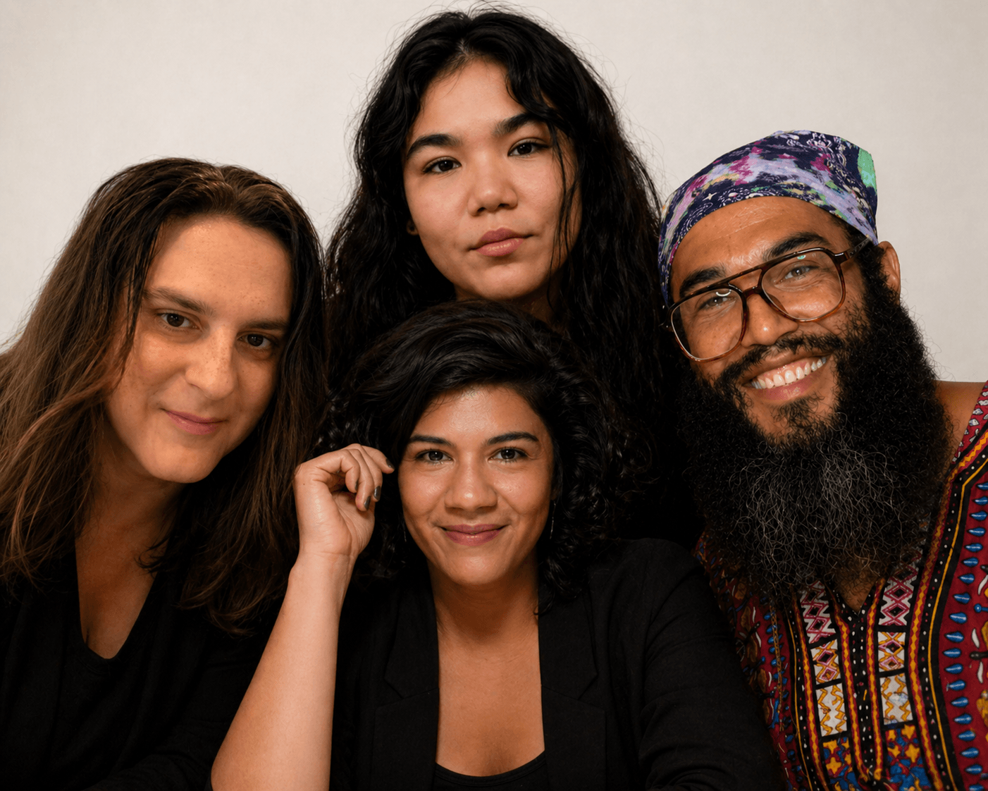 Four people smiling, posing closely together against a plain background.