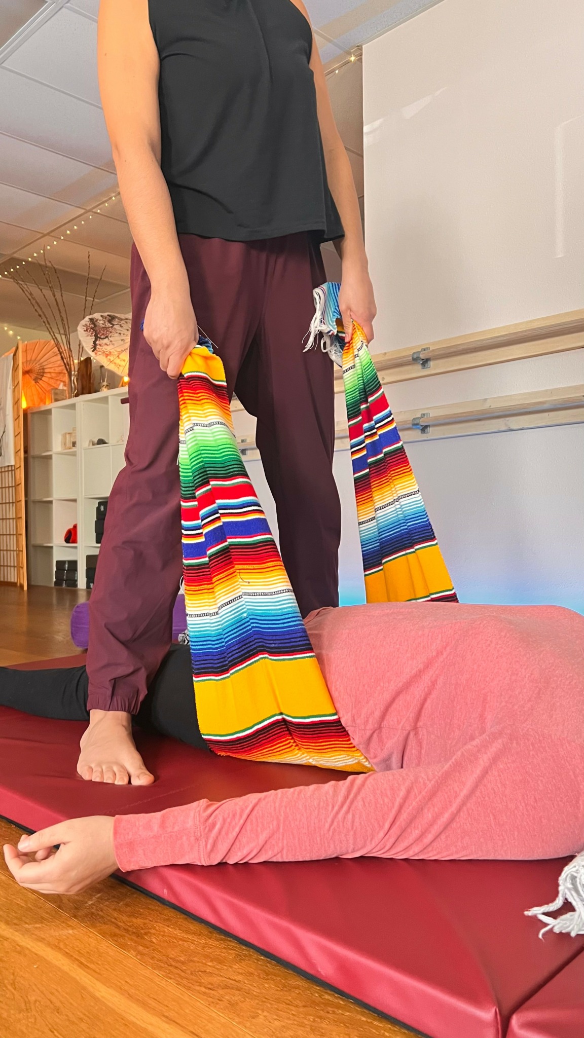 Person standing on a pink cushion holding colorful striped bags, indoors with furniture and warm lighting.