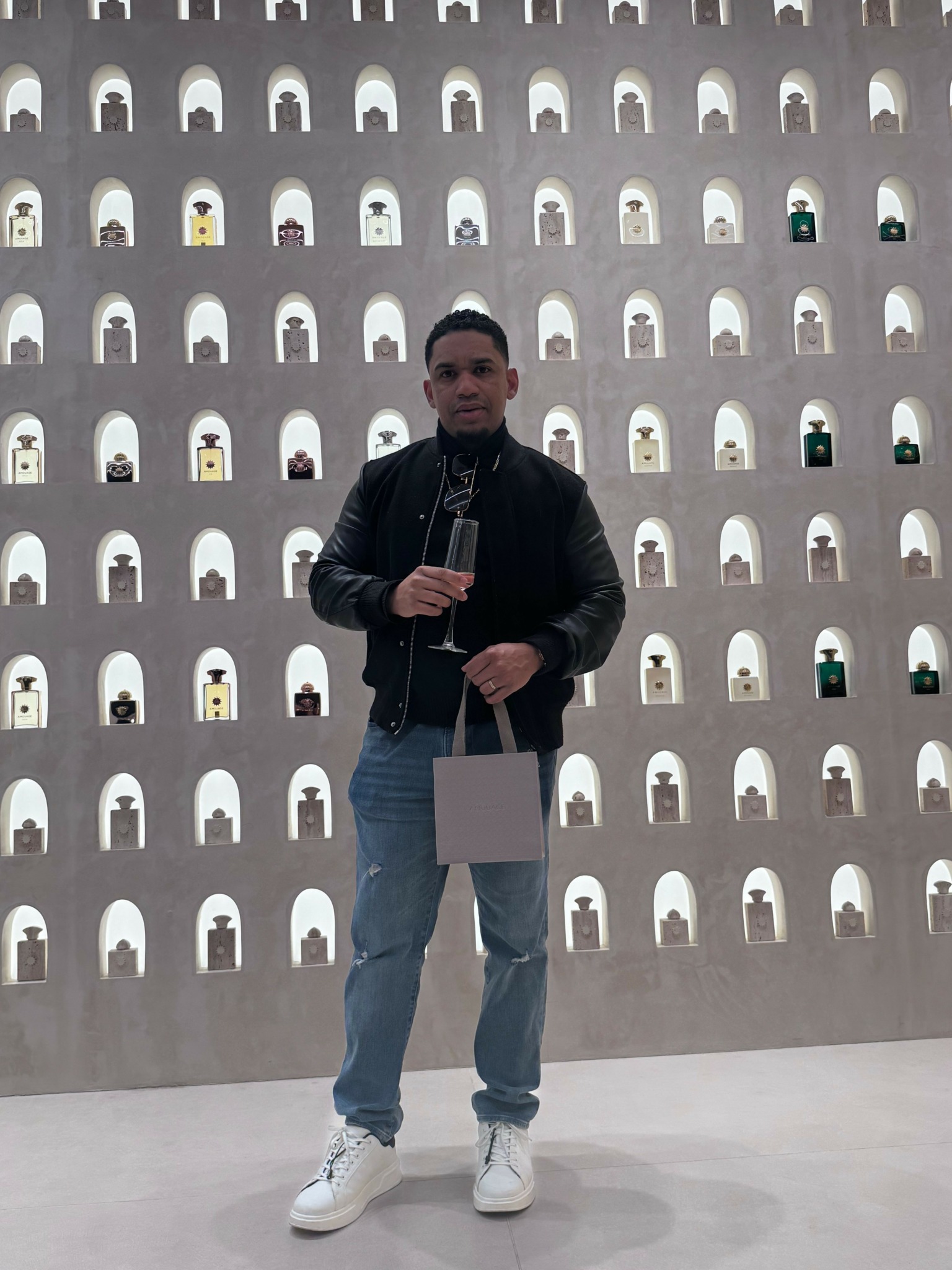 Person standing in front of a wall with numerous small, white, arched objects, holding a tablet and a bag.