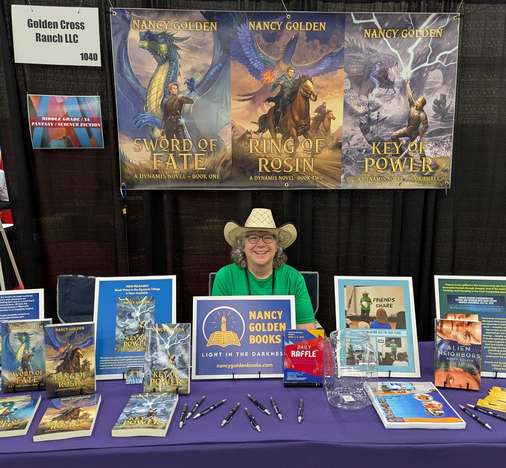 Woman with glasses and cowboy hat sitting at a book table with Nancy Golden Books sign, books, and pens.
