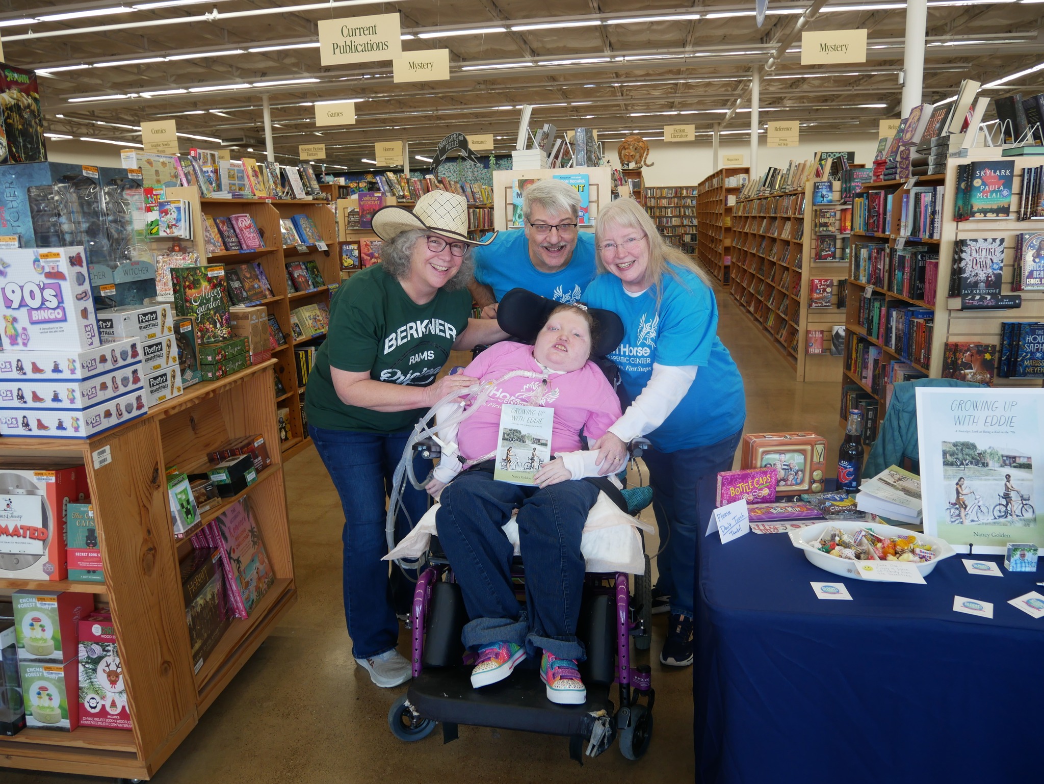 Four people in a bookstore, one in a wheelchair, smiling and posing together.
