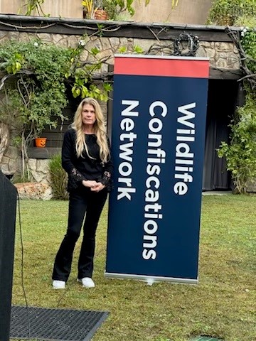 Woman with long blonde hair standing outdoors next to a large sign with text about confidentiality and network, in a grassy area.
