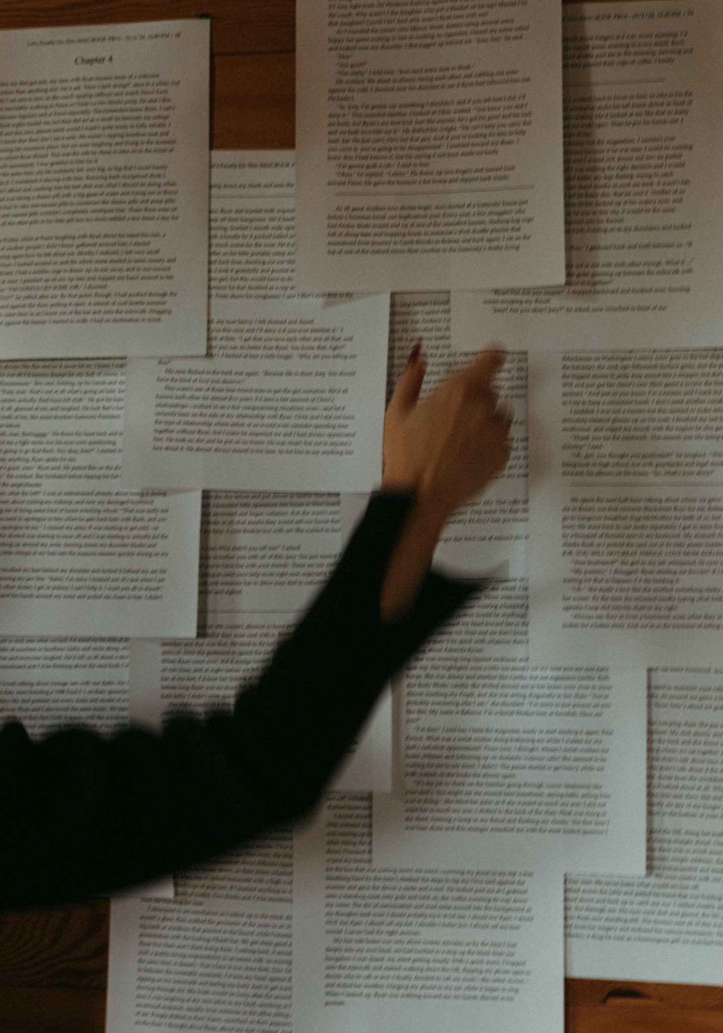 Person's hand reaching for papers spread on a table, with multiple documents visible.