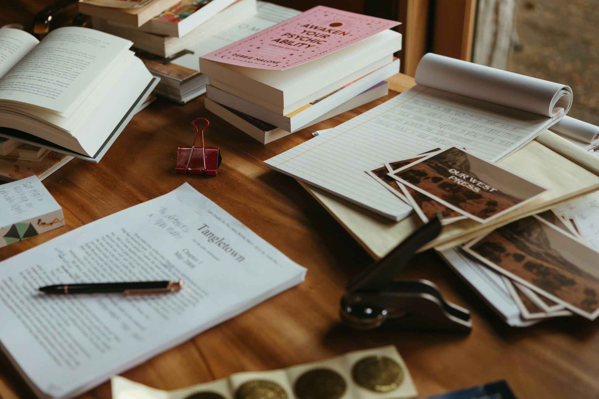 Desk with open books, notebooks, photographs, and office supplies on wooden surface.