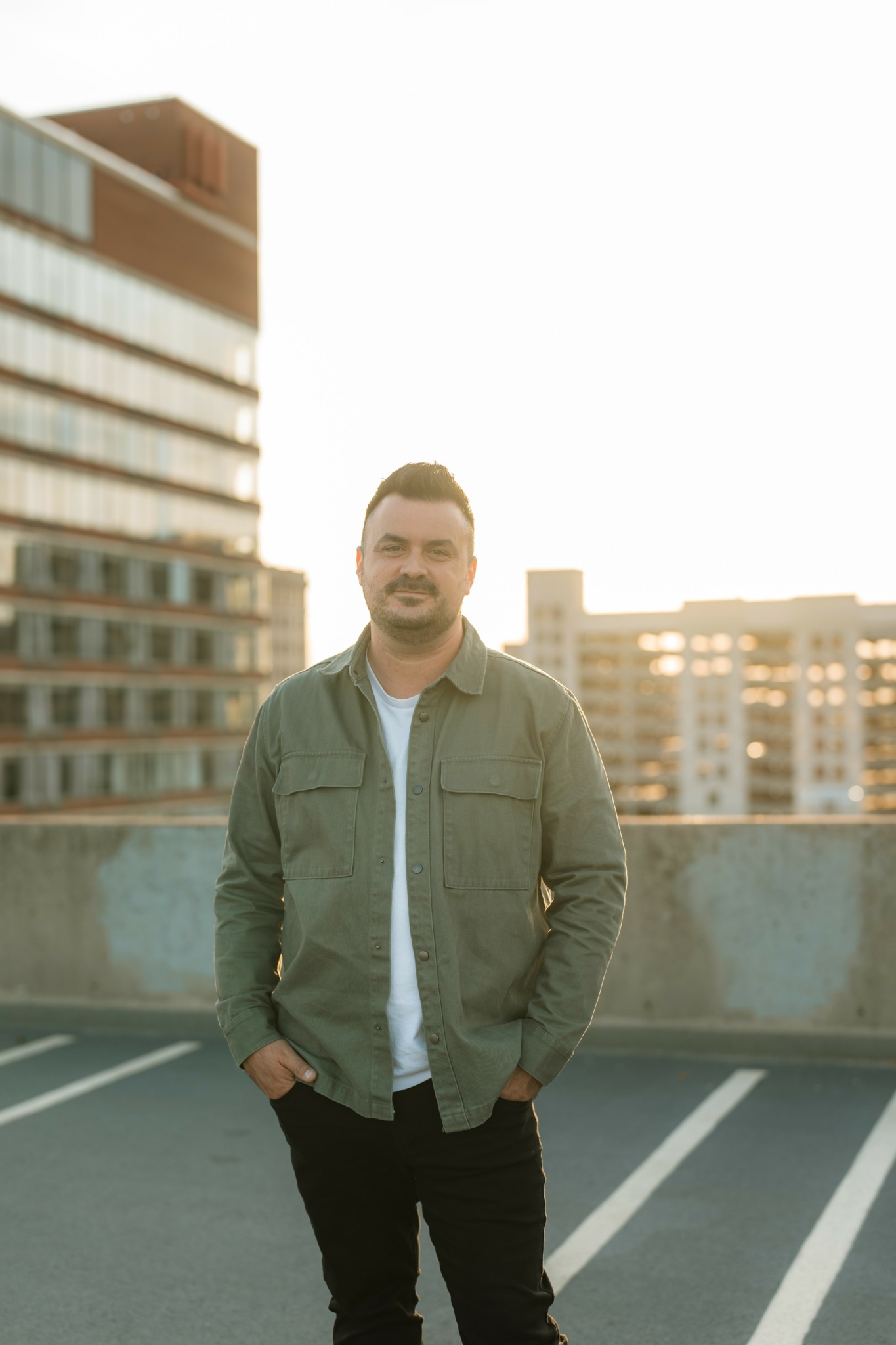 Man standing on rooftop parking lot with city buildings in background during sunset.
