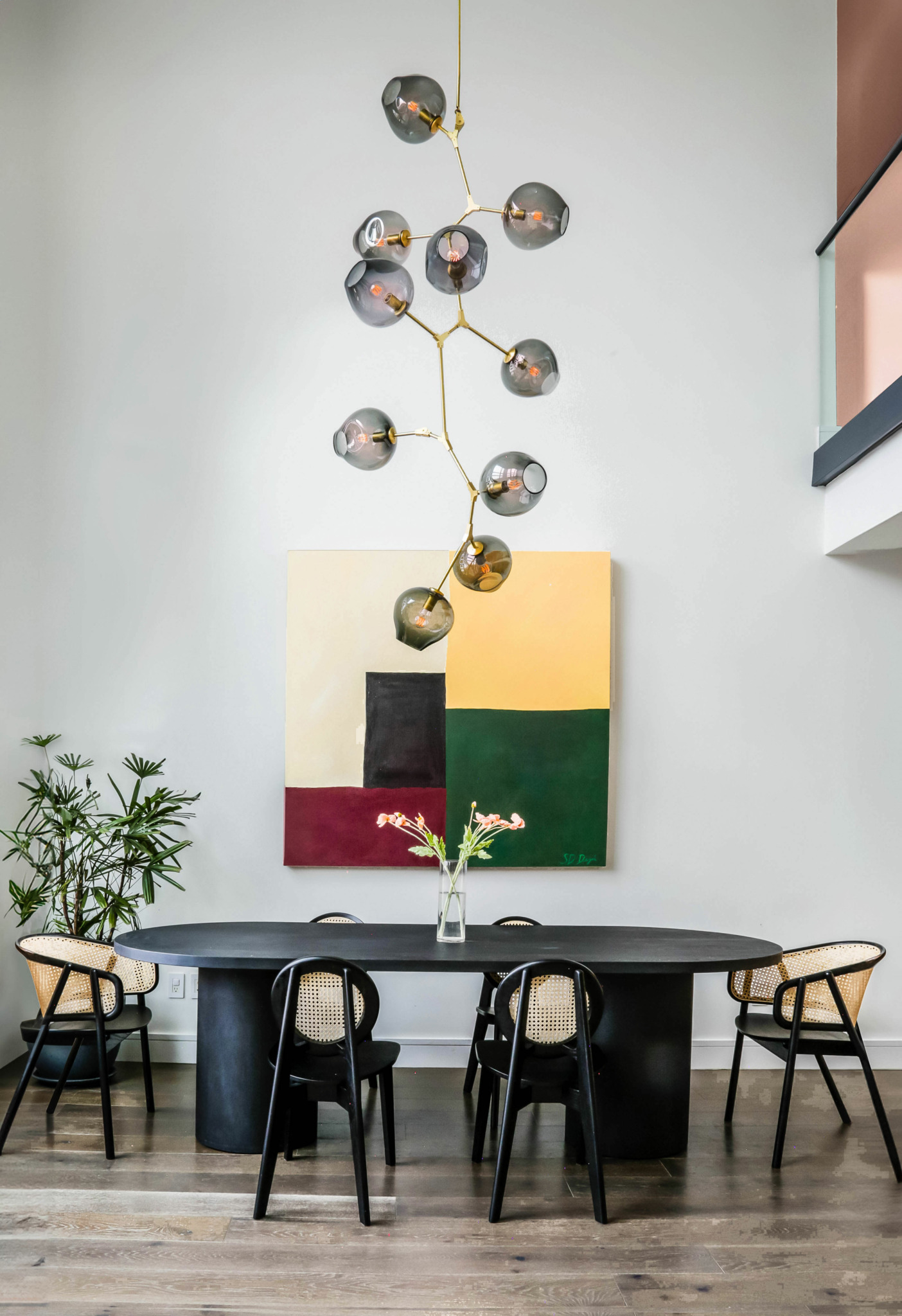Dining area with a black table, four chairs, a plant, and a colorful abstract painting on the wall.