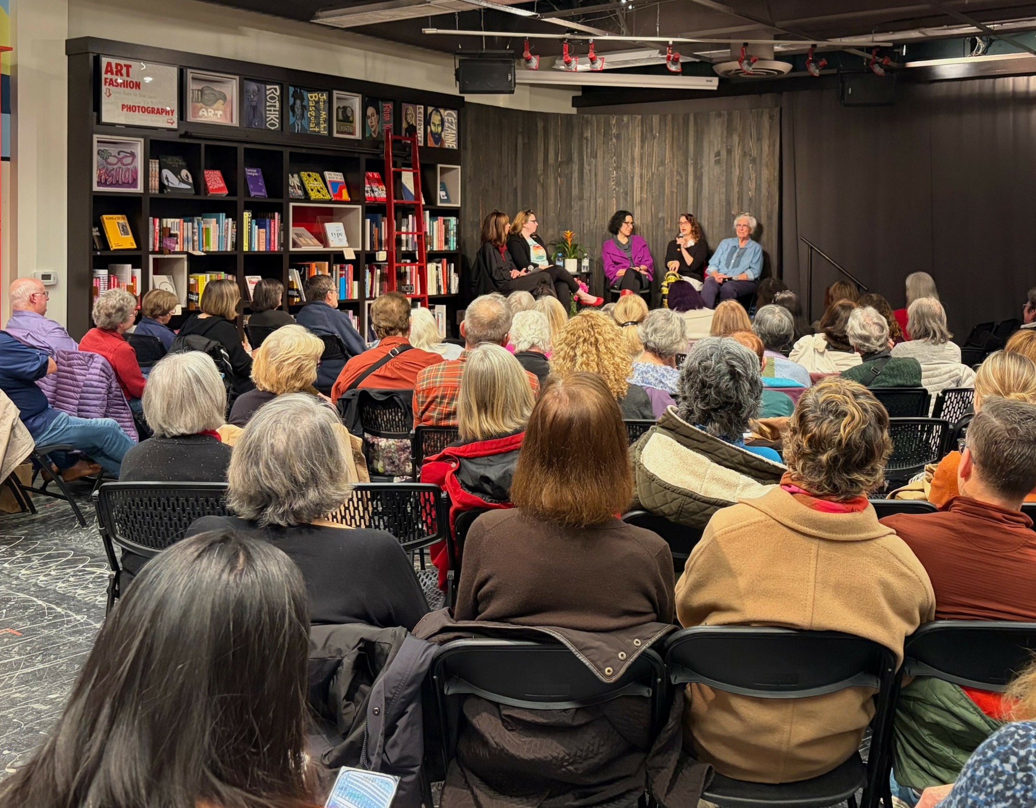 Panel discussion with four people on stage in front of an audience in a room with bookshelves.