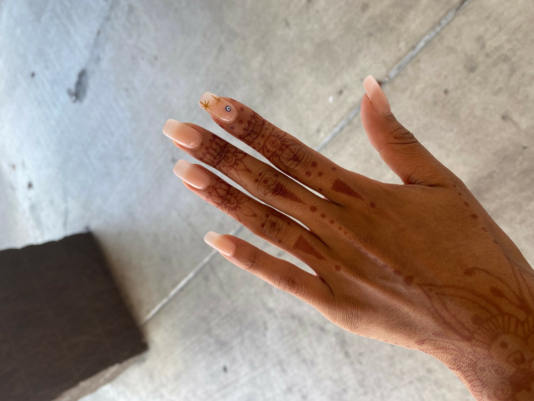 Hand with henna designs, fingers extended, outdoors surface in background.
