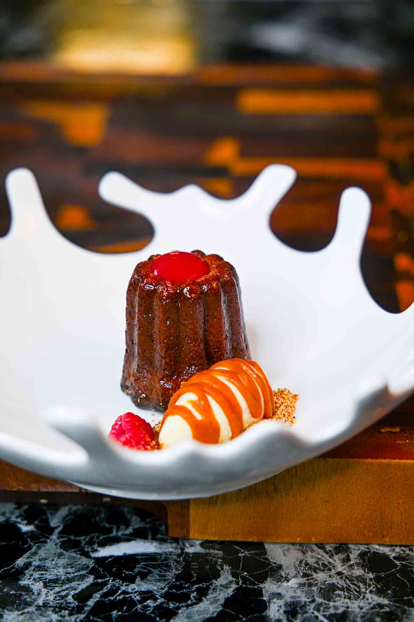 Chocolate dessert topped with red fruit, surrounded by orange and white candies and small red berries in a white bowl.