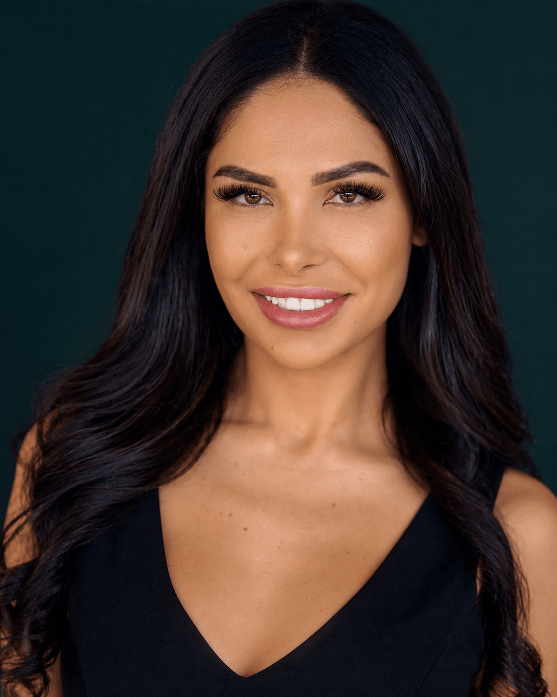 Young woman with long dark hair, smiling, wearing a black V-neck top, against a dark background.