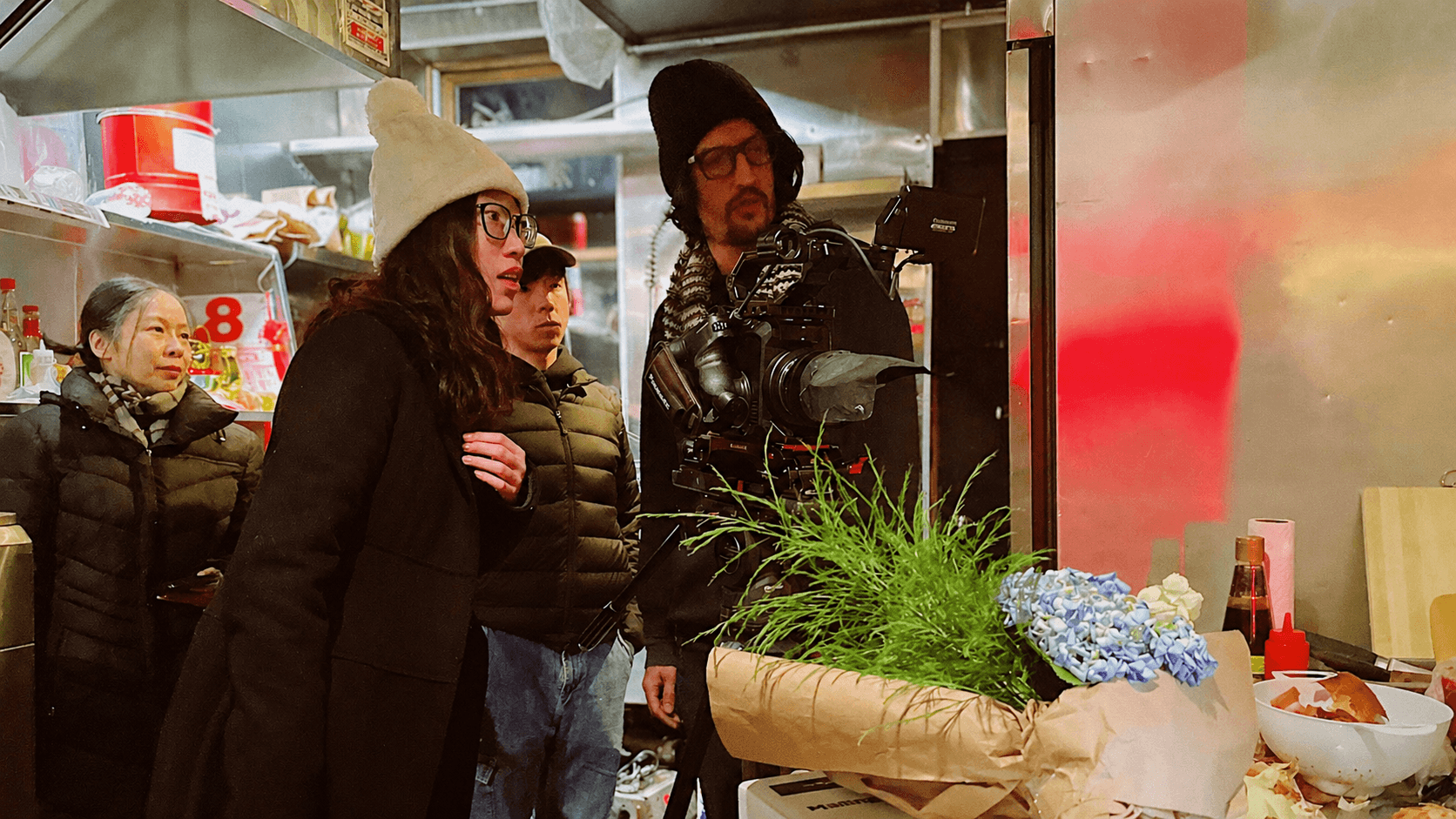Group of people in a store, with a man operating a camera and a woman looking at plants and flowers.
