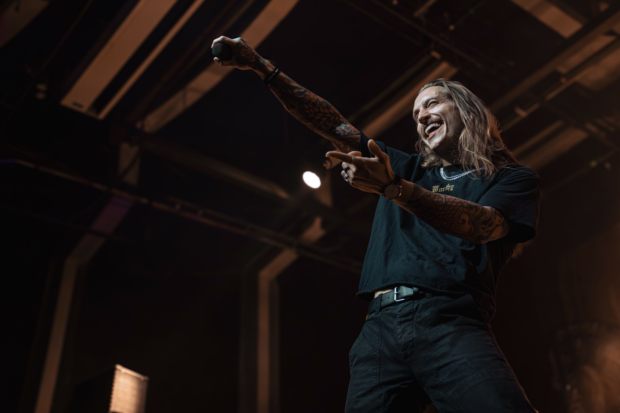Person smiling and pointing with one arm raised on stage in a dark setting.