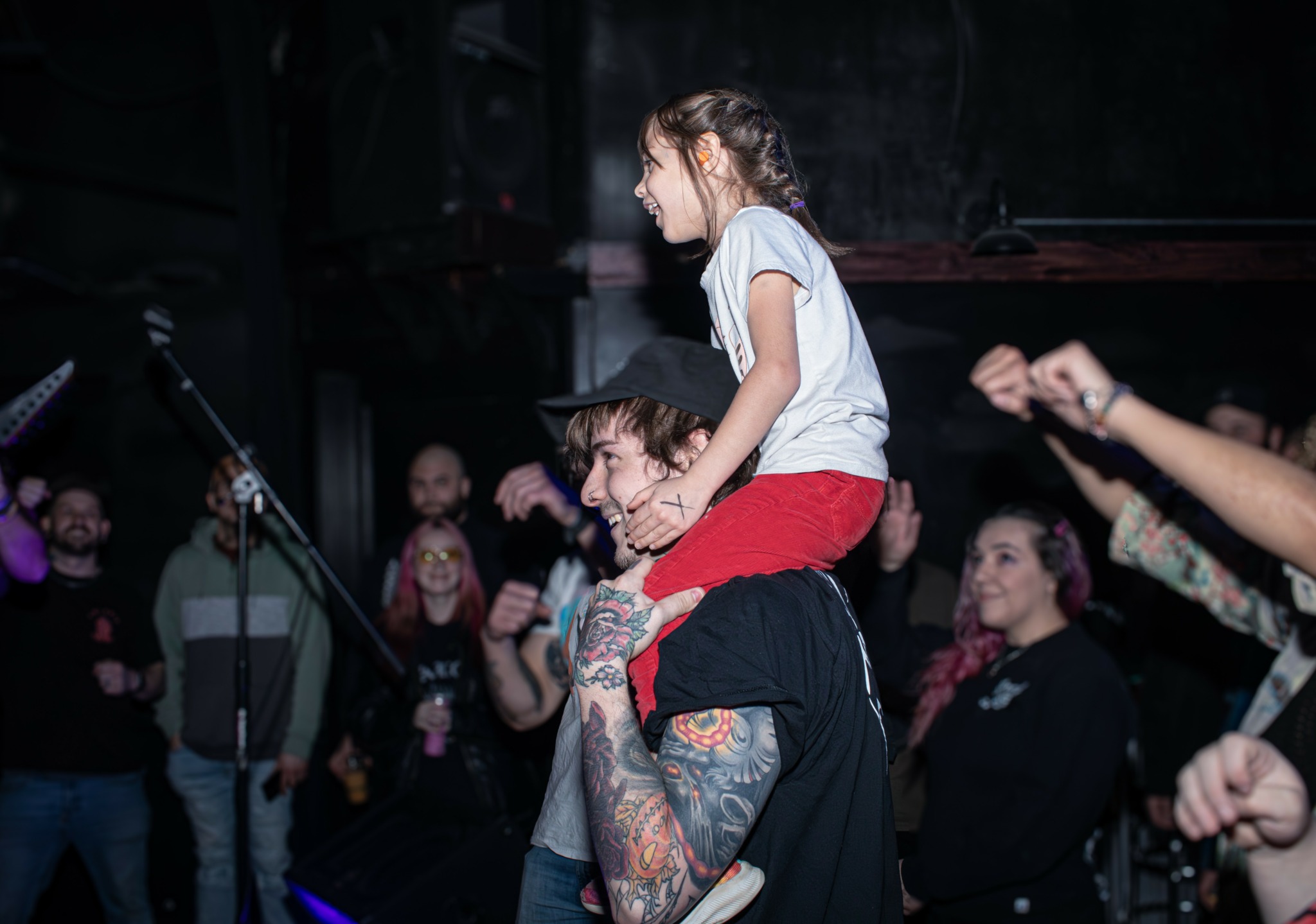 Child sitting on a person's shoulders at a crowded indoor event, with people watching and taking photos.