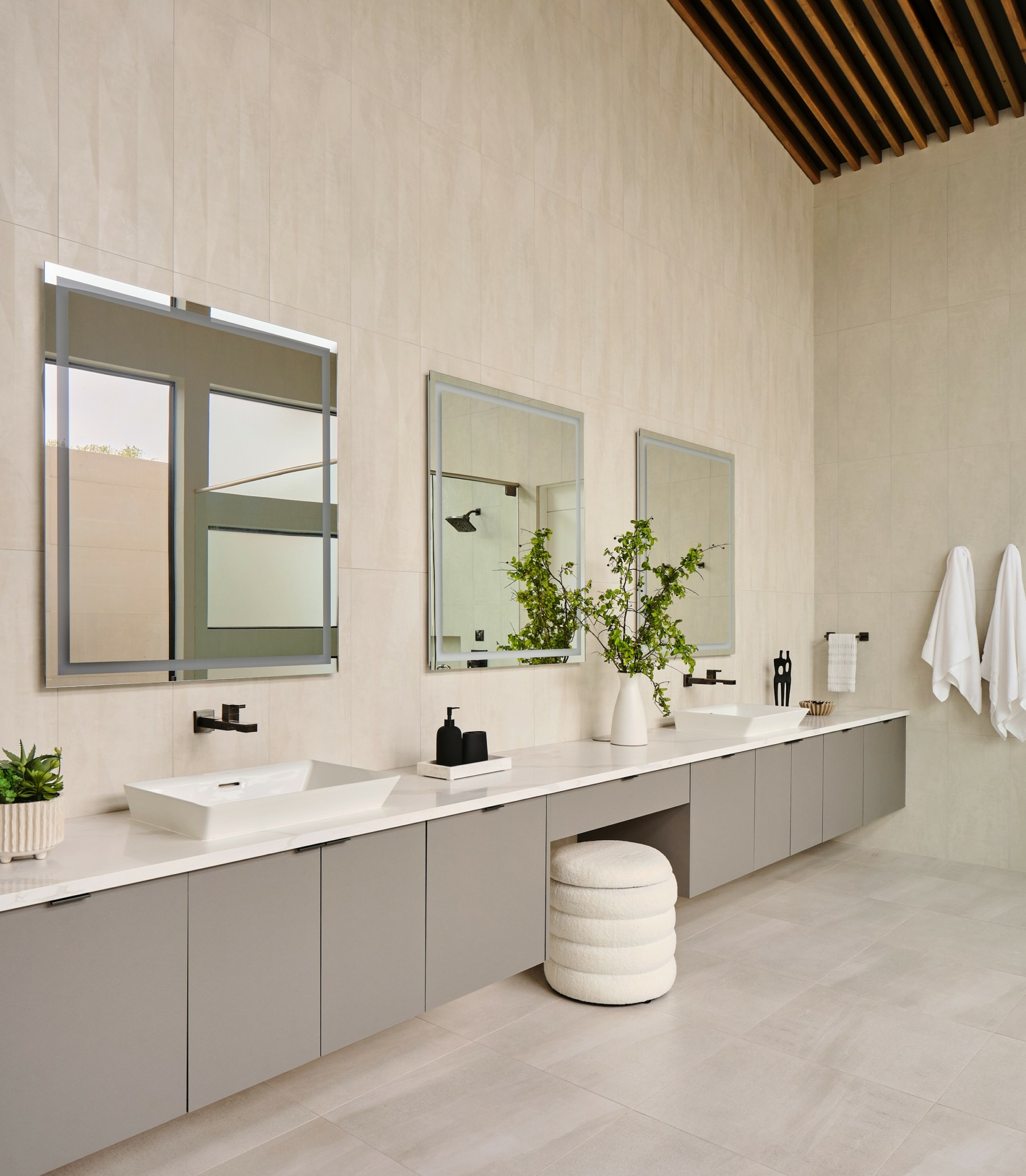Modern bathroom with two sinks, three mirrors, potted plants, and white towels on wall hooks.