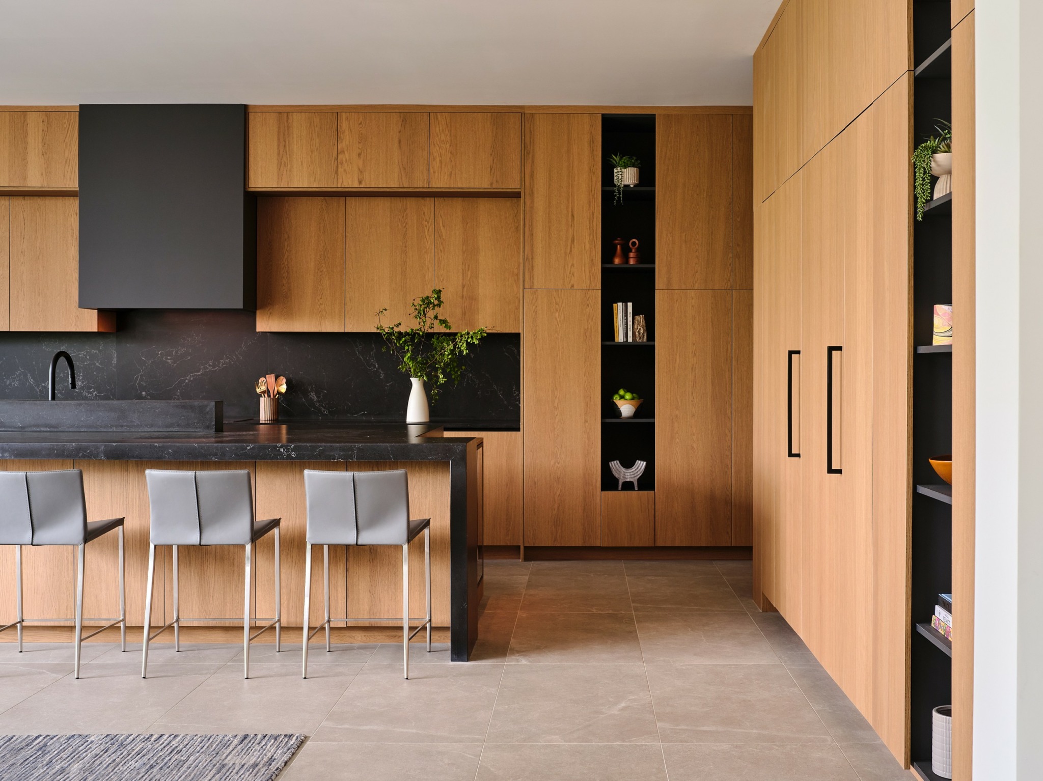 Modern kitchen with wooden cabinets, black countertop, and four gray chairs at a breakfast bar.