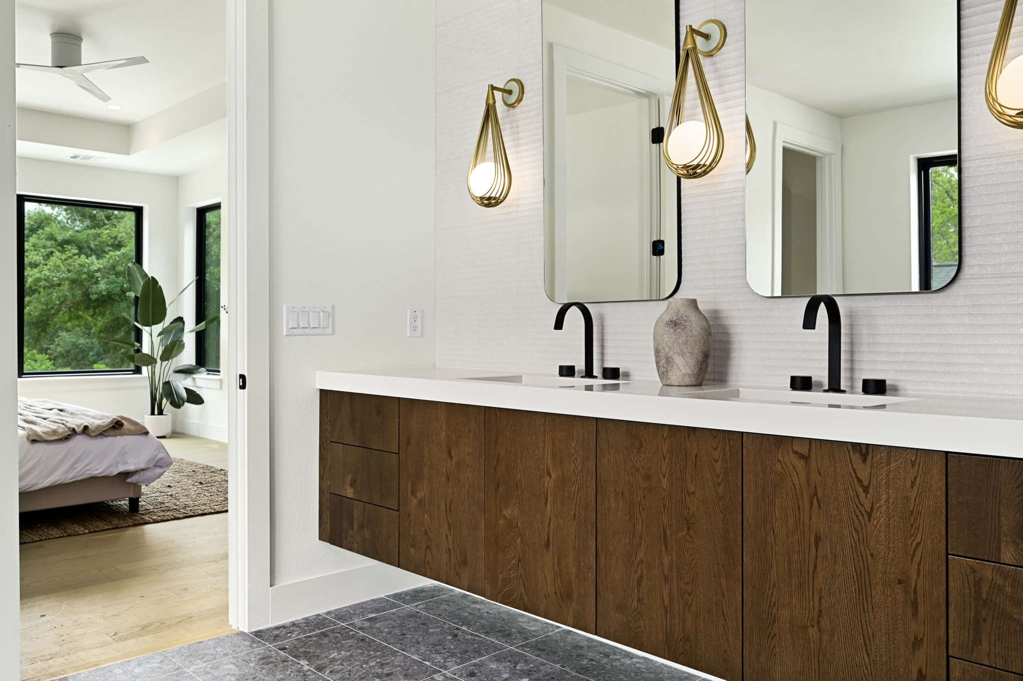 Modern bathroom with double sinks, mirrors, pendant lights, and a wooden vanity, adjacent to a bedroom with large windows.
