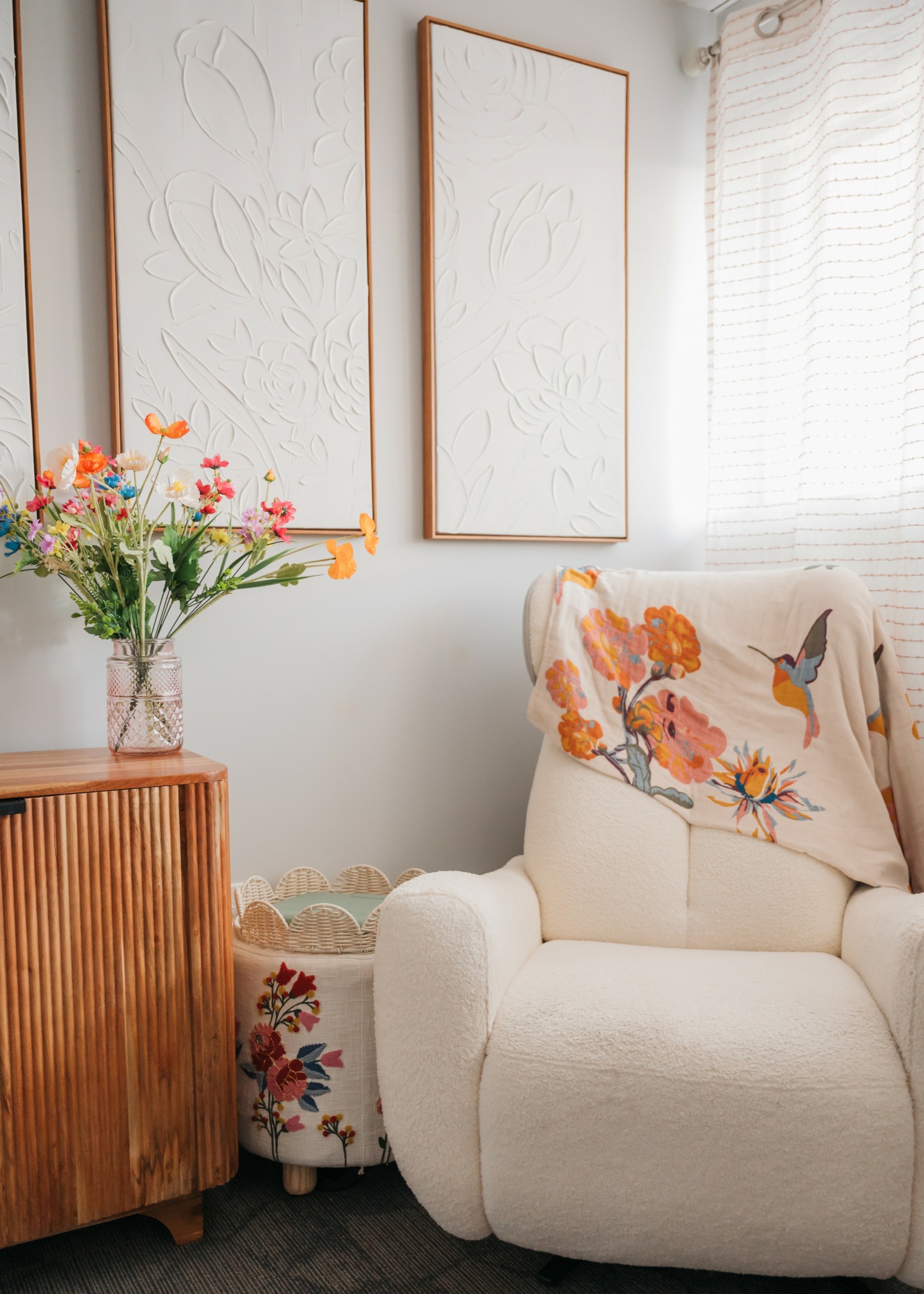 Living room corner with a white sofa, floral pillow, wooden cabinet, and framed artwork on the wall.