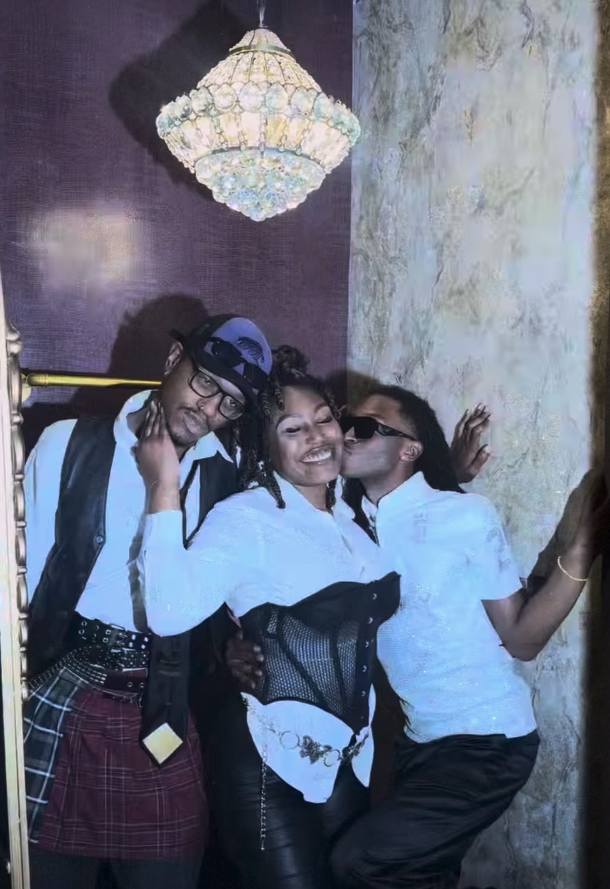 Three people smiling and posing together indoors, with a chandelier hanging above them.