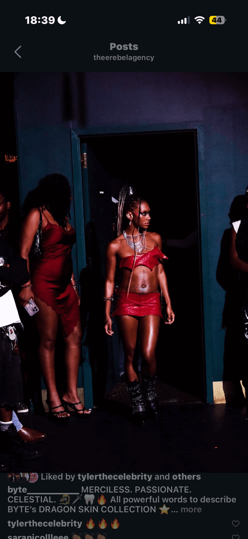 Person in red outfit standing in a dark room with others nearby, some partially visible, in a club or event setting.