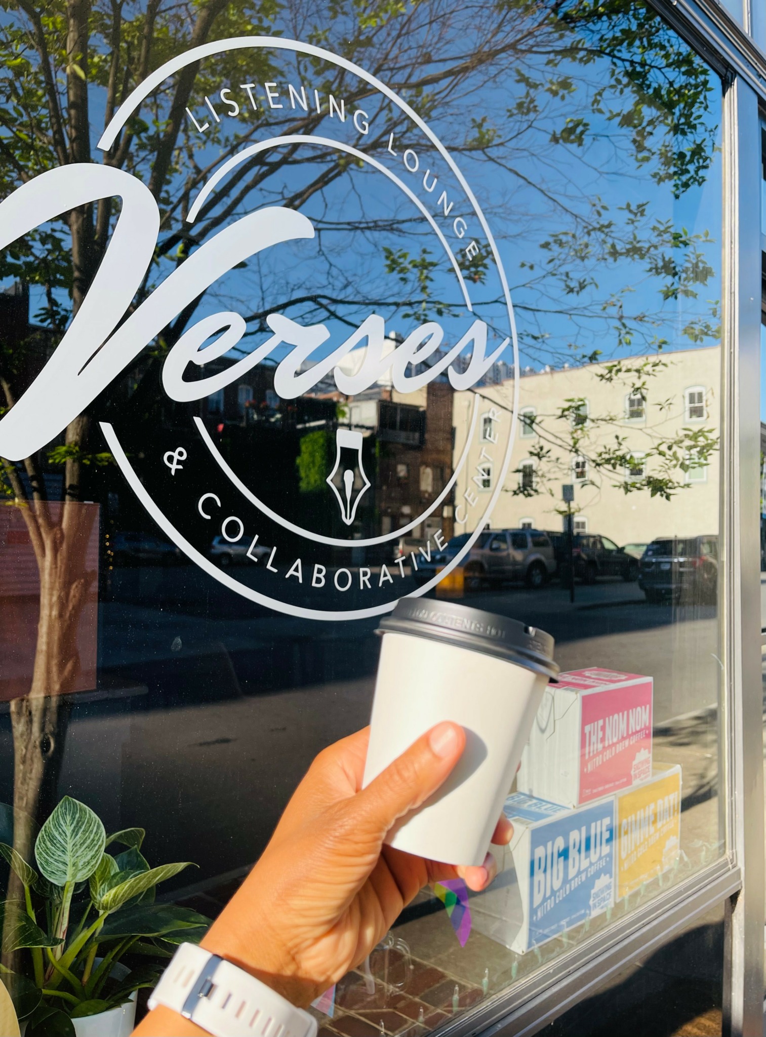 Person holding a coffee cup outside a window with a logo reading 'Listening, Looking, Verus, & Collaborating'.