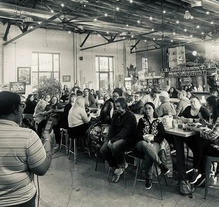 People sitting at tables in a busy cafe or restaurant, with large windows and industrial-style ceiling.