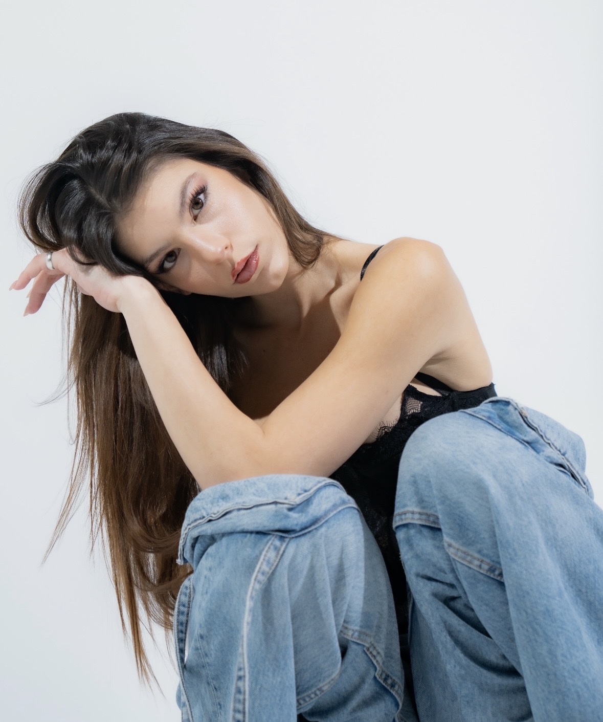 Woman with long hair resting her head on her arm, wearing a black top and blue jeans.
