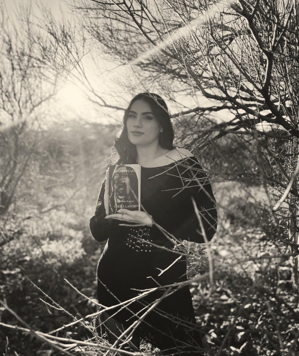 Woman holding a glass award outdoors with trees and sunlight in background.