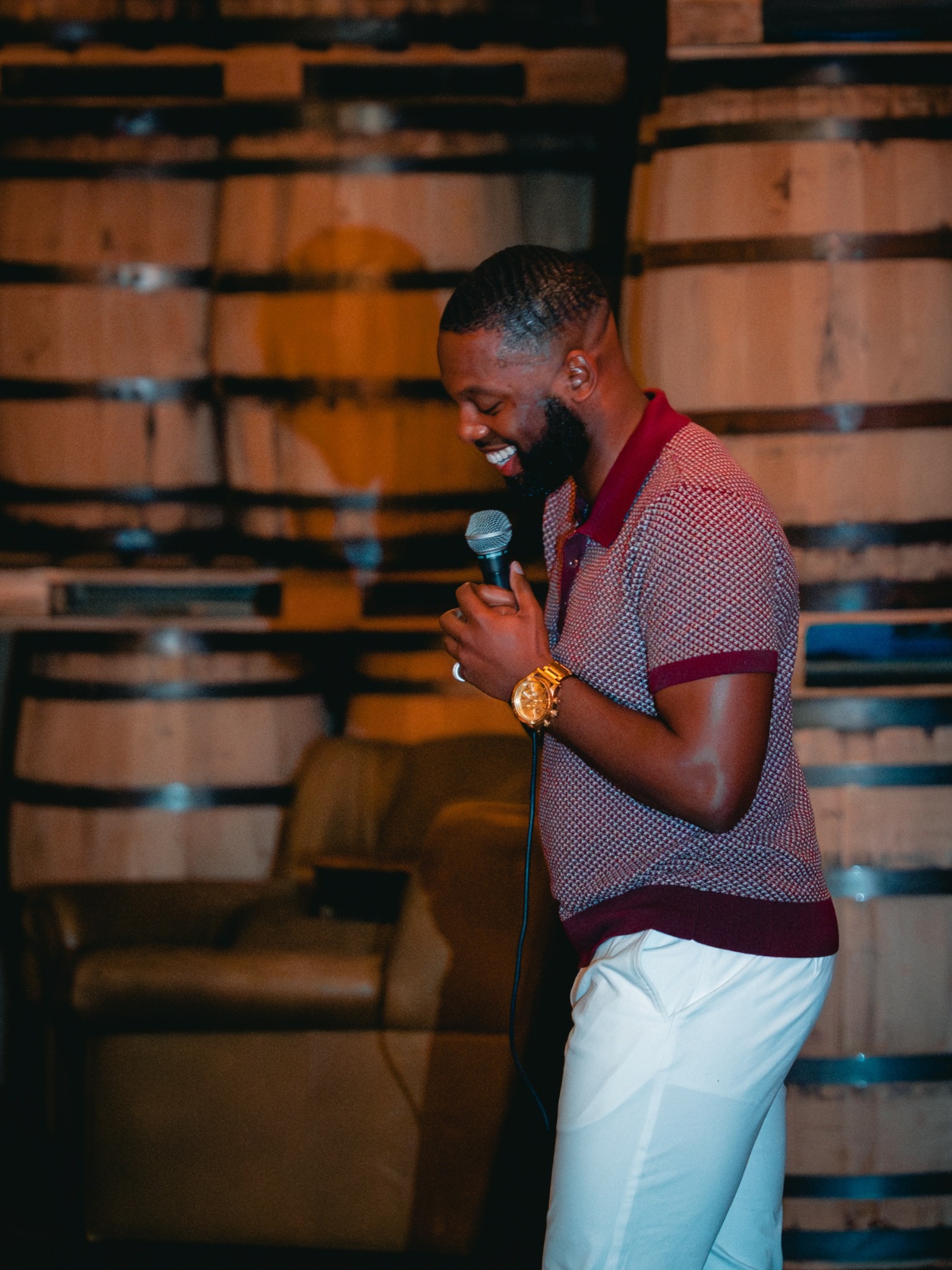 Man holding microphone, smiling, standing indoors with wooden wall background.