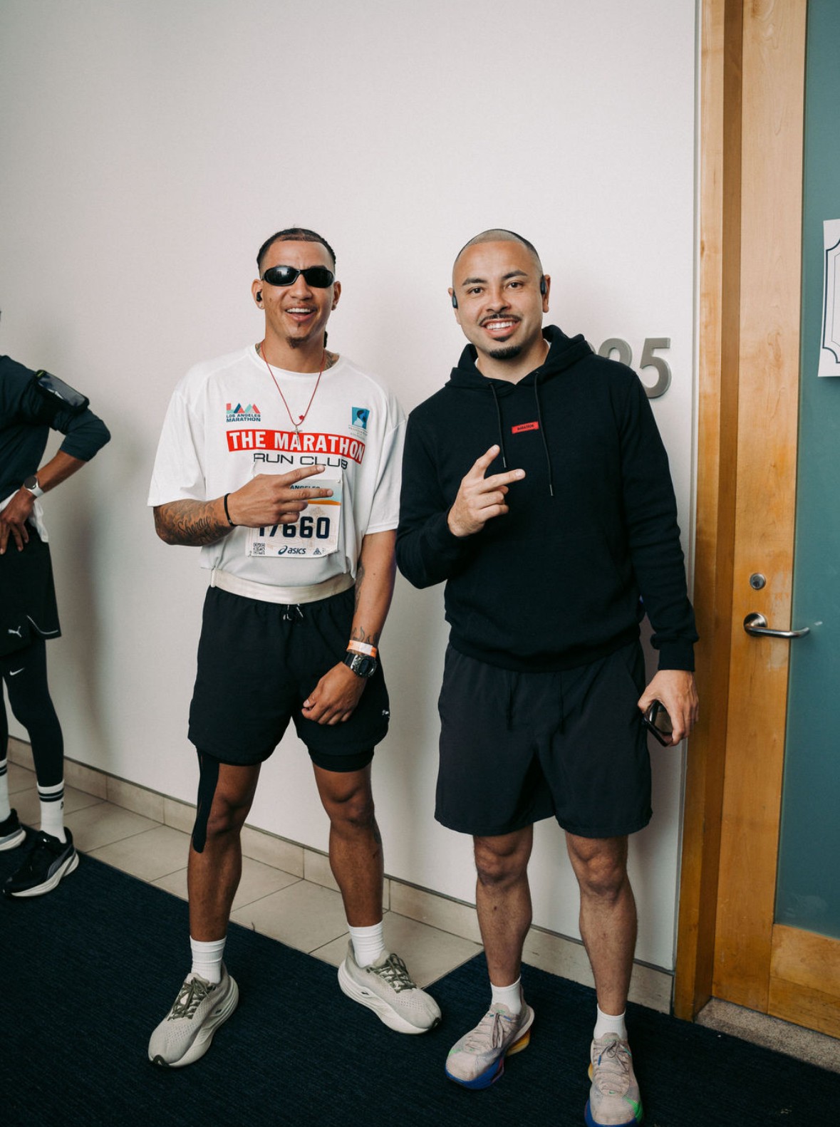 Two men standing indoors, smiling, making peace signs, wearing athletic clothing and sunglasses.