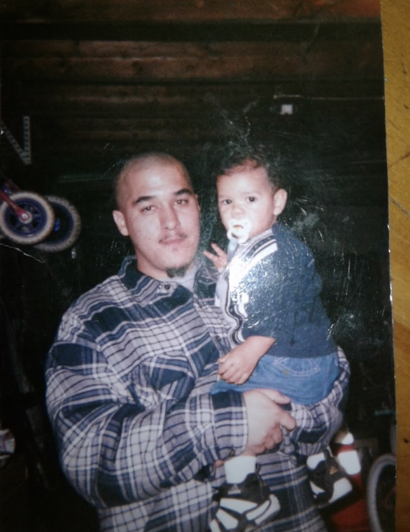 Adult holding a child indoors with dark wooden background, both looking at the camera.