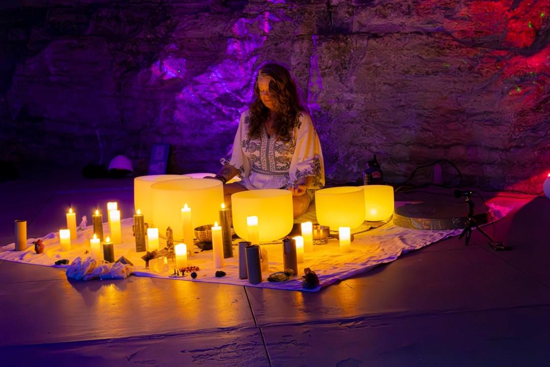 Person standing behind illuminated bowls and candles on a table in a dimly lit space with colorful lighting.