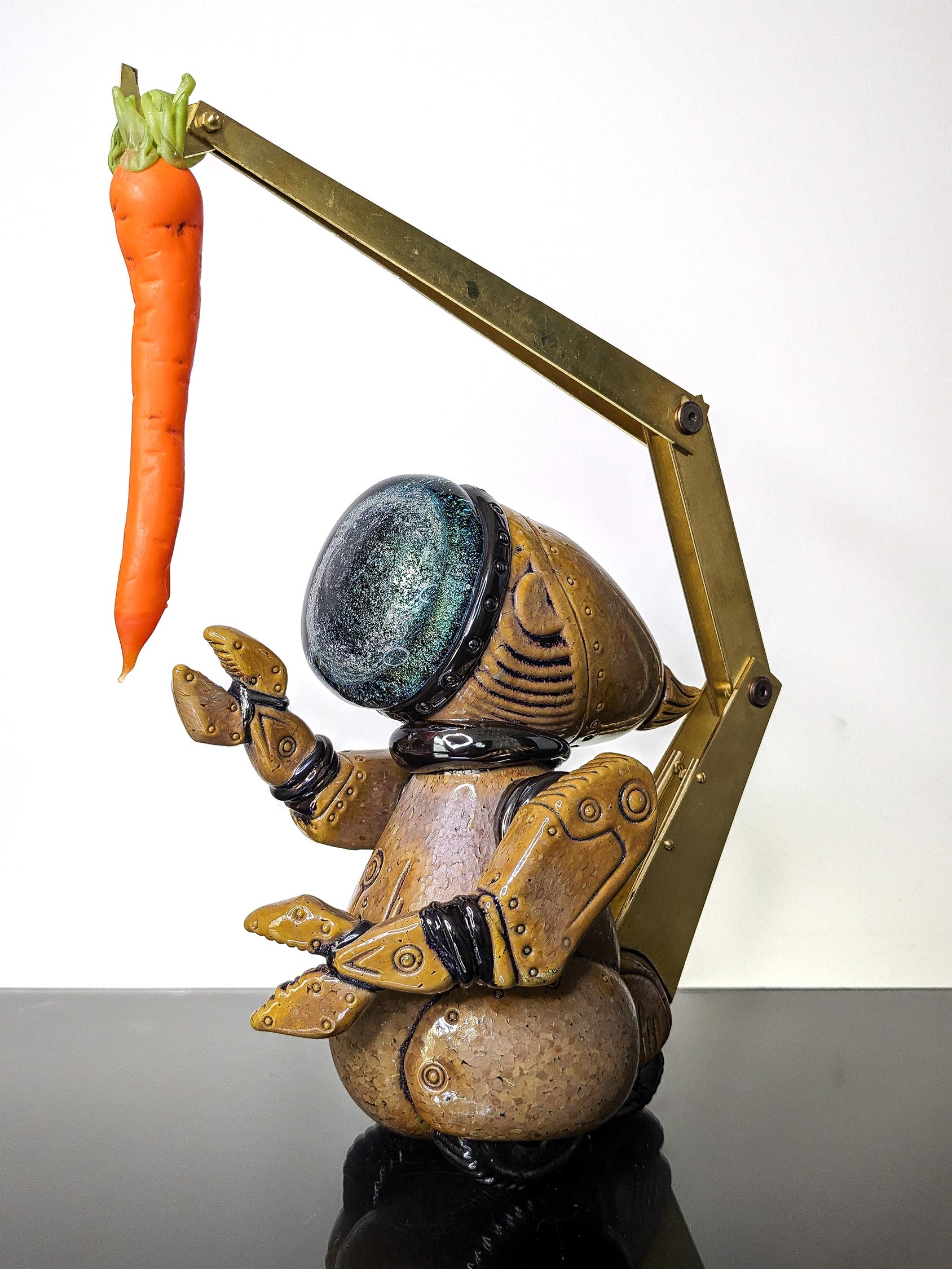 Robot holding a carrot with a robotic arm, standing on a black surface against a white background.