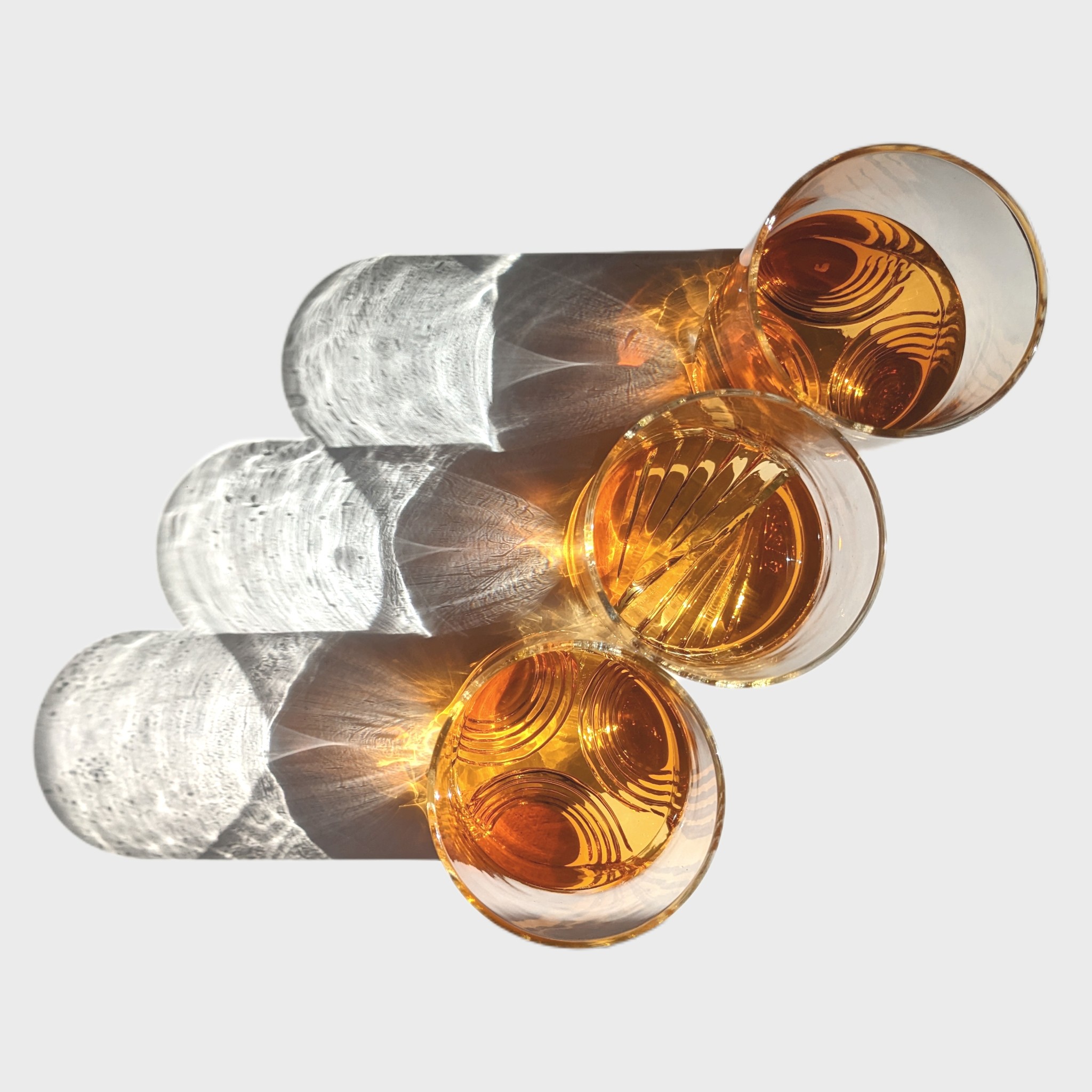 Four glasses, two clear and two amber, arranged on a white surface with shadows and reflections.