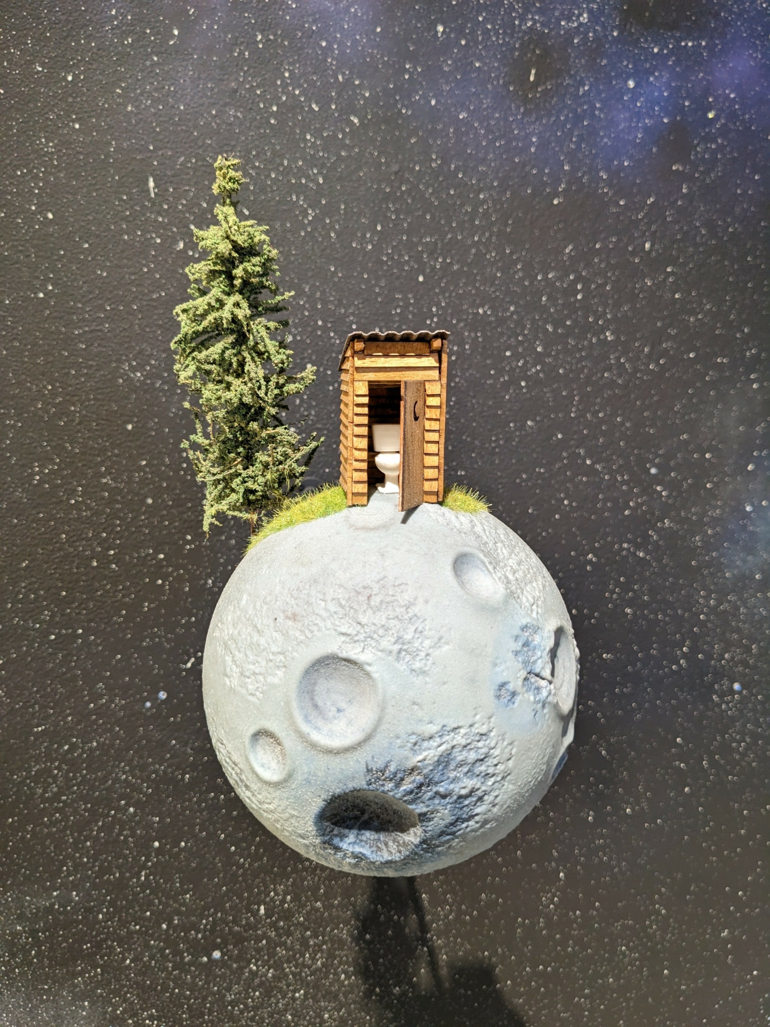 Miniature moon with a door, tree, and starry sky background.