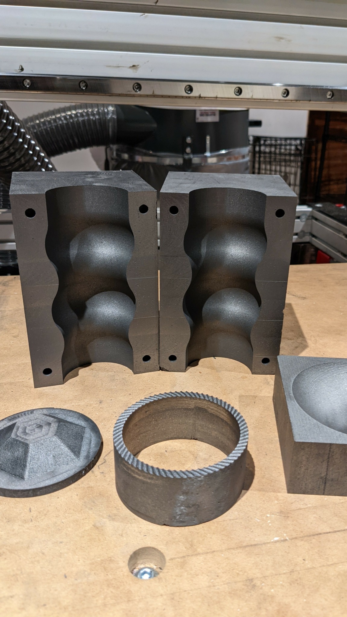 Two black, curved, symmetrical objects with multiple rounded indentations, placed vertically side by side on a wooden surface.