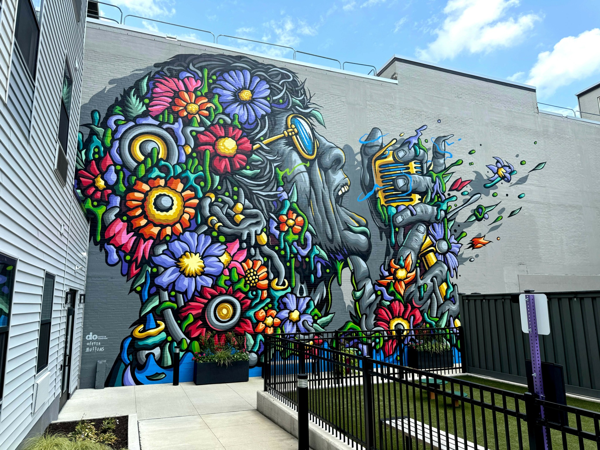 Colorful mural of flowers and abstract shapes on a building wall, with a blue sky background.