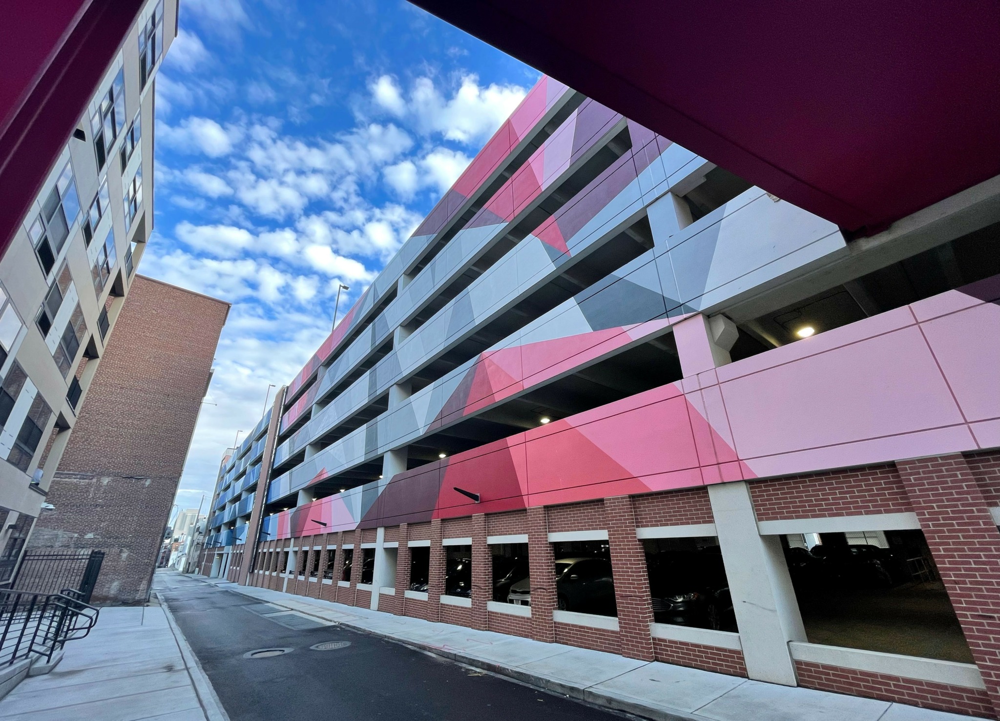 Modern multi-story building with pink and white exterior, blue sky with clouds, and a street view.