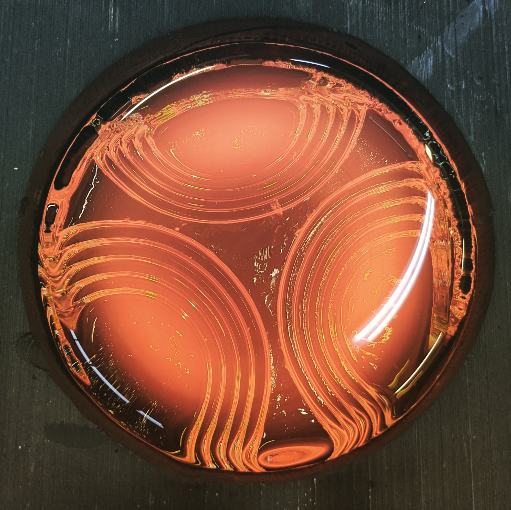 Circular object with glowing orange and red swirling patterns inside, on a dark surface.