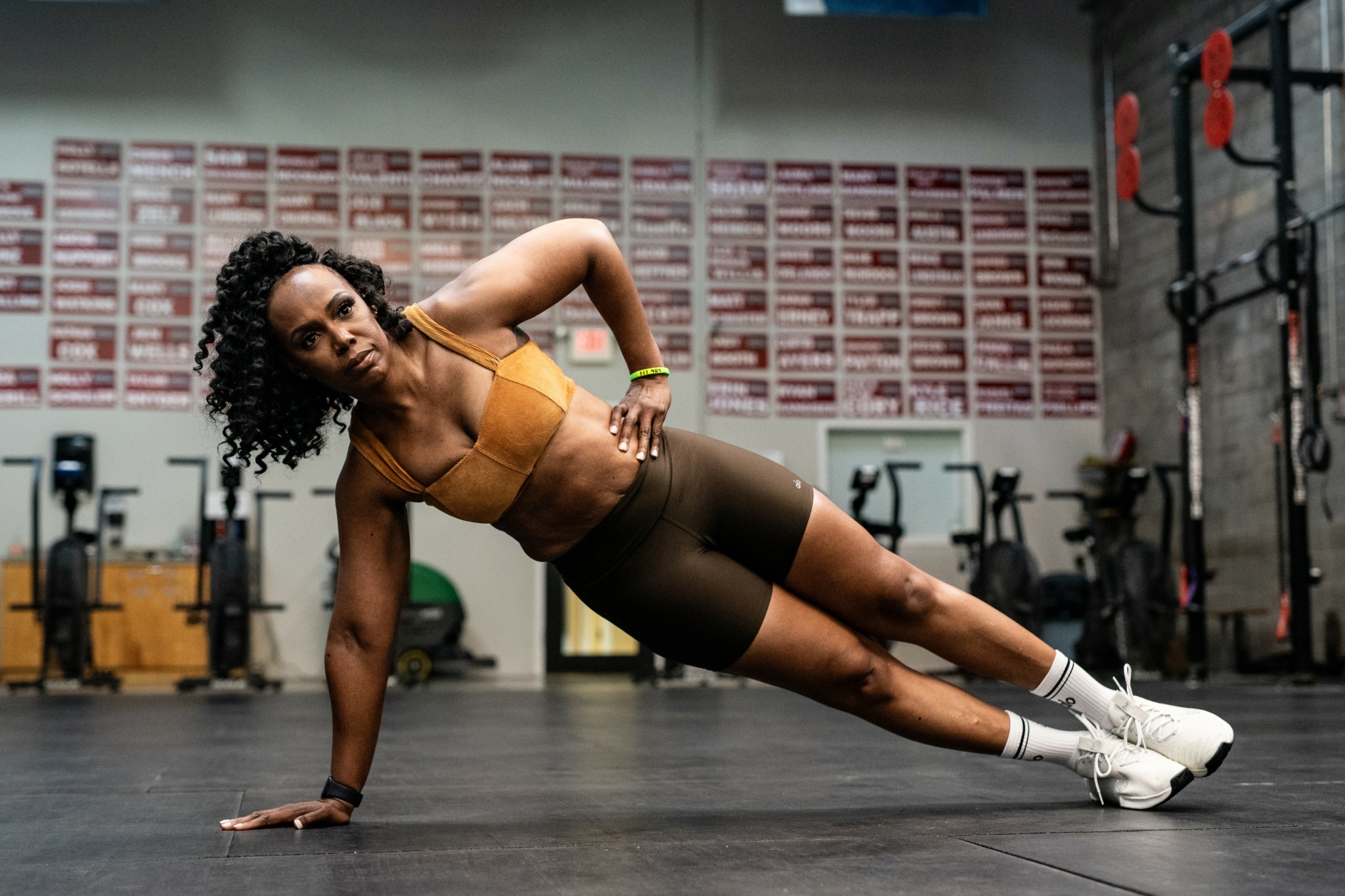 Woman in workout clothes performing side plank exercise in gym with equipment and wall posters.