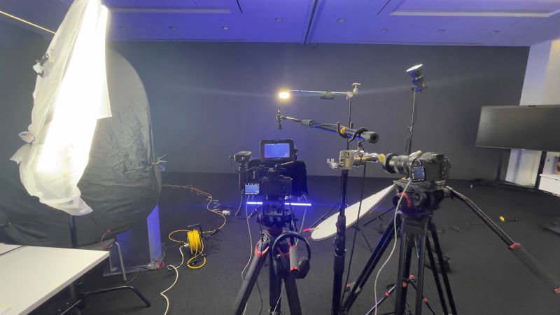 Laboratory setup with cameras, equipment, and a person in the background, illuminated by bright and blue lighting.