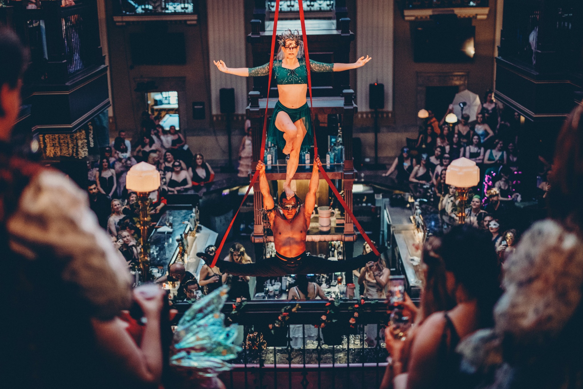 Two performers in a circus act, one upside down and one supporting, surrounded by an audience in a theater.