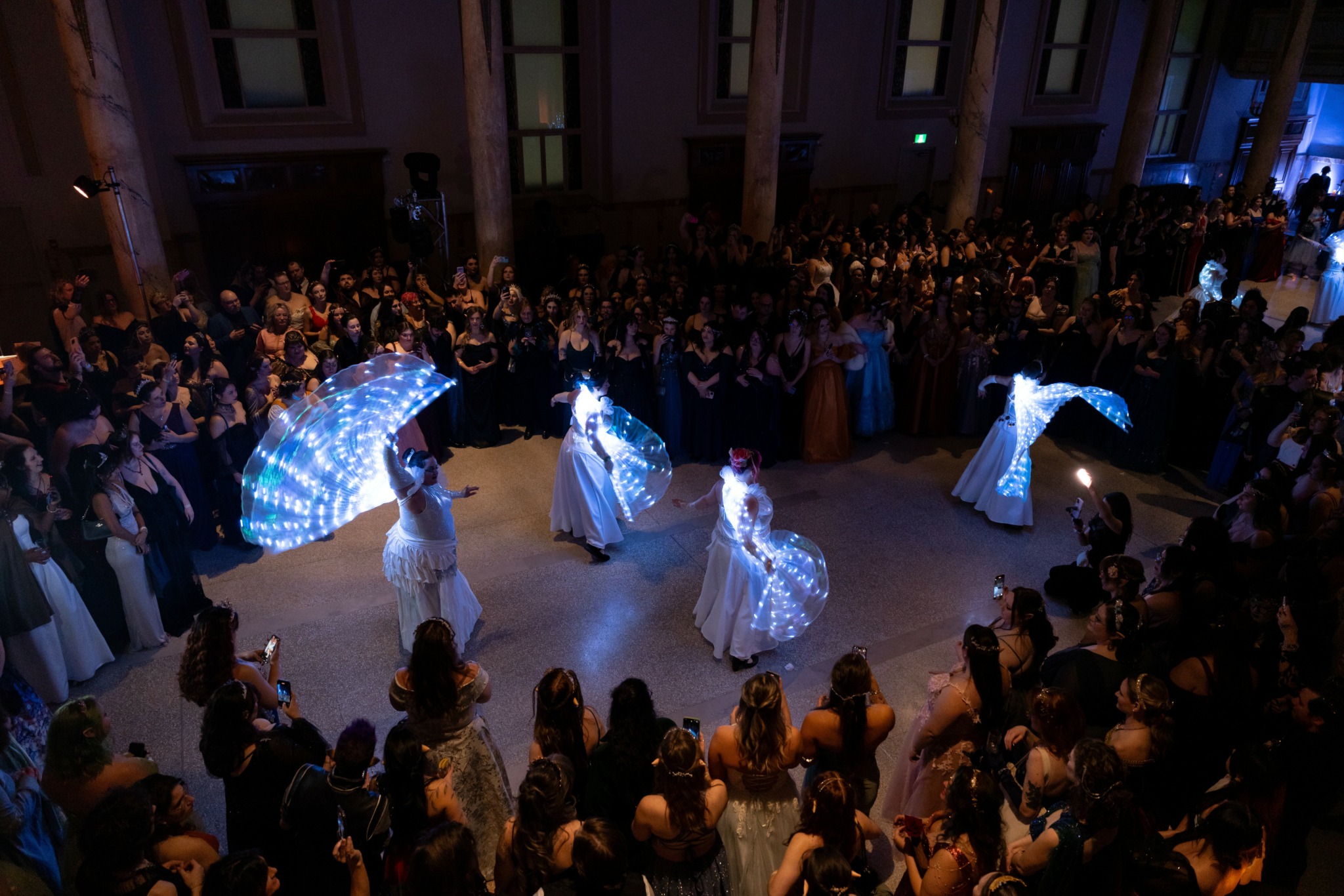 Five performers with illuminated umbrellas dance in front of a large audience in a spacious hall.