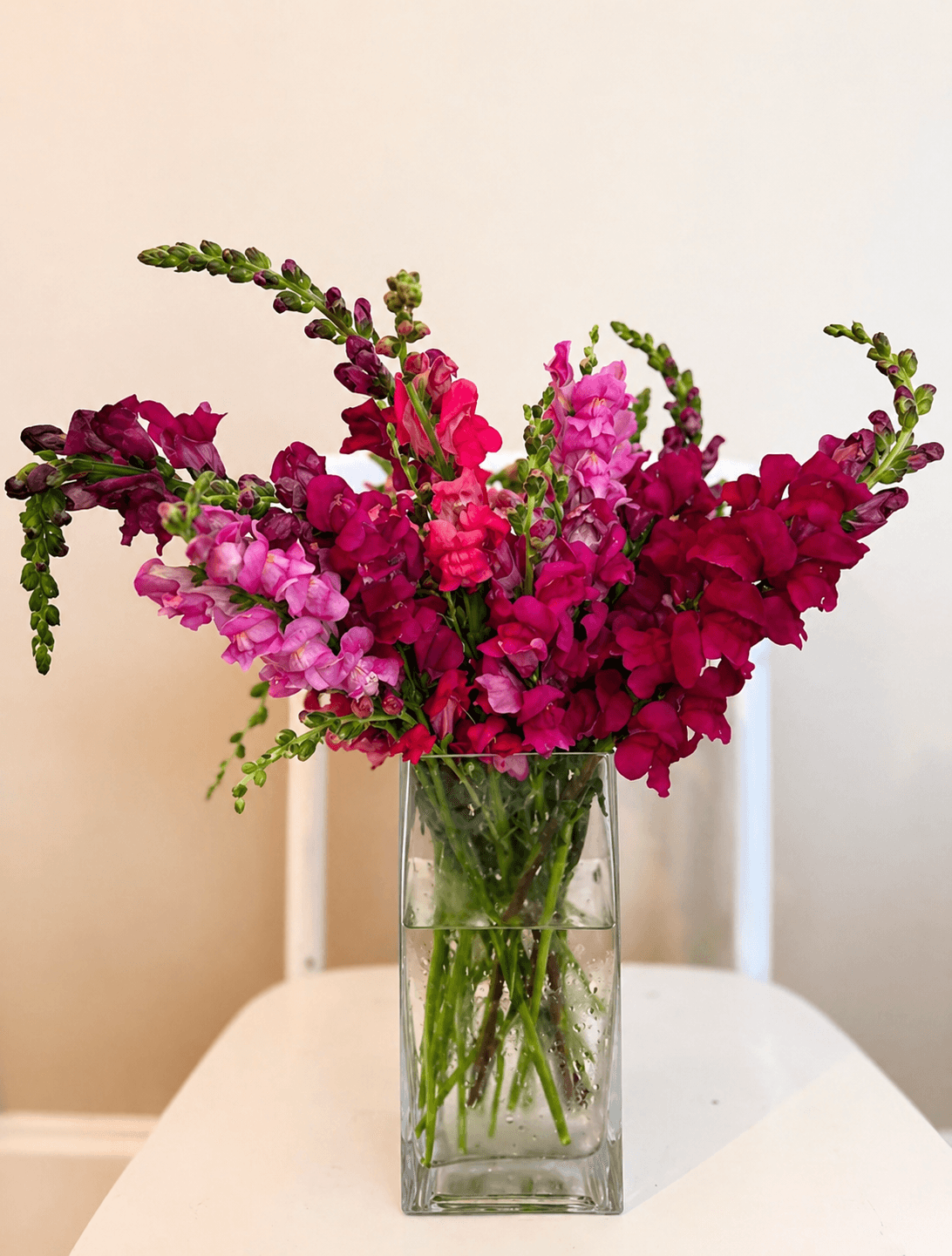 Vase with pink and purple flowers on a white table against a plain background.