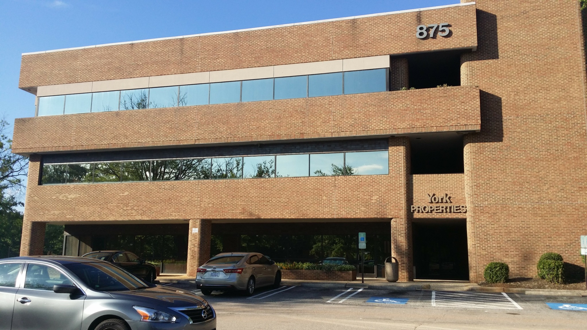 Modern brick building with large glass windows and parking lot in front.