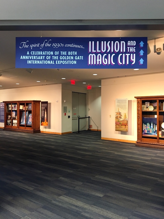 Indoor space with display cases and a sign about an illusion and magic city exhibit.